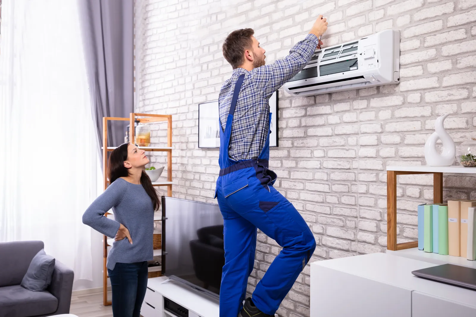young,woman,looking,at,male,technician,repairing,air,conditioner,mounted