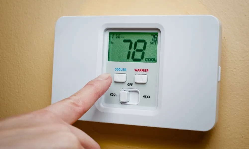 a hand setting the thermostat in a cooler temperature